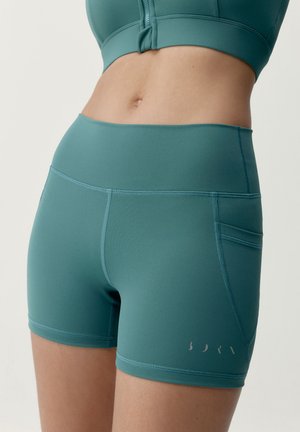 Turquoise hoge taille sportshorts met zijzak op de rechterdij, gedragen met bijpassend cropped zip-up topje, getoond op torso en bovenbenen.