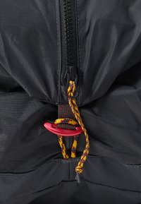 Schwarze Stoffjacke mit einem Reißverschluss in der Mitte. Verfügt über eine bunte Kordel mit einem roten Stopper und strukturiertem Stich rund um die Kanten.