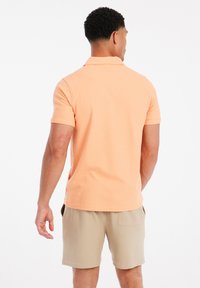 Licht oranje polo shirt met korte mouwen en kraag, gecombineerd met beige shorts. Zachte textuur, casual pasvorm en geen zichtbare patronen.