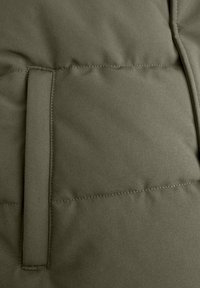 Olijfgroen gewatteerde stof met een zachte textuur, voorzien van een zijvak met een gestikt randje en een strakke, minimalistische uitstraling.