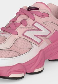 Ροζ και λευκό αθλητικό παπούτσι New Balance με πλέγμα, χοντρή σόλα και ροζ κορδόνια σε λευκό φόντο.