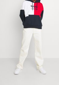 Felpa con cappuccio a blocchi di colore in blu navy, rosso e bianco con una tasca frontale e cappuccio con coulisse, abbinata a jeans a gamba dritta color avorio e sneakers bianche.