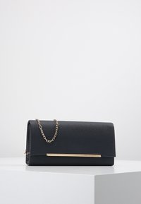 Sac à main noir texturé avec une chaîne dorée et un accent métallique à l'avant, doté d'une fermeture à rabat.