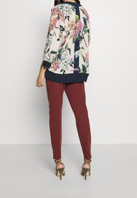 Floral patterned blouse in light fabric with navy accents, paired with slim burgundy pants and strappy metallic high-heeled sandals.