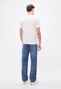 Camiseta blanca de algodón con mangas cortas, combinada con jeans de mezclilla azul de corte holgado y ligero desgaste, usada con zapatillas blancas.
