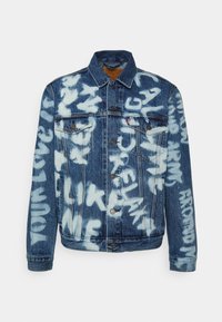 Veste en jean avec fermeture à boutons et poches poitrine, avec des motifs de texte blanc style graffiti sur le devant, les manches et les épaules.