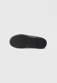 Black sneaker sole with a textured, pattern design. Features "SKECHERS" logo and curved edges, enhancing grip and durability.
