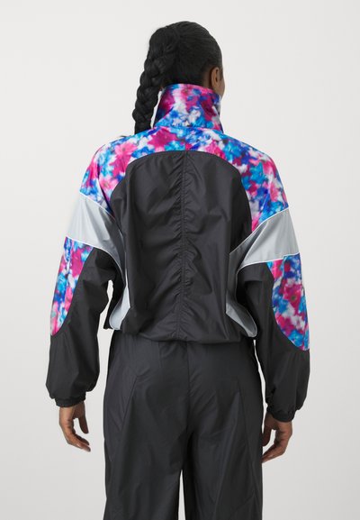 Veste coupe-vent colorée présentant une base noire avec des accents tie-dye vibrants en rose et bleu, un col haut et des poignets élastiques.