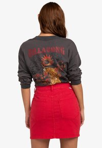 Chemise grise à manches longues avec un motif léopard et un graphisme de soleil rouge, associée à une mini-jupe en denim rouge vif avec des poches arrière.