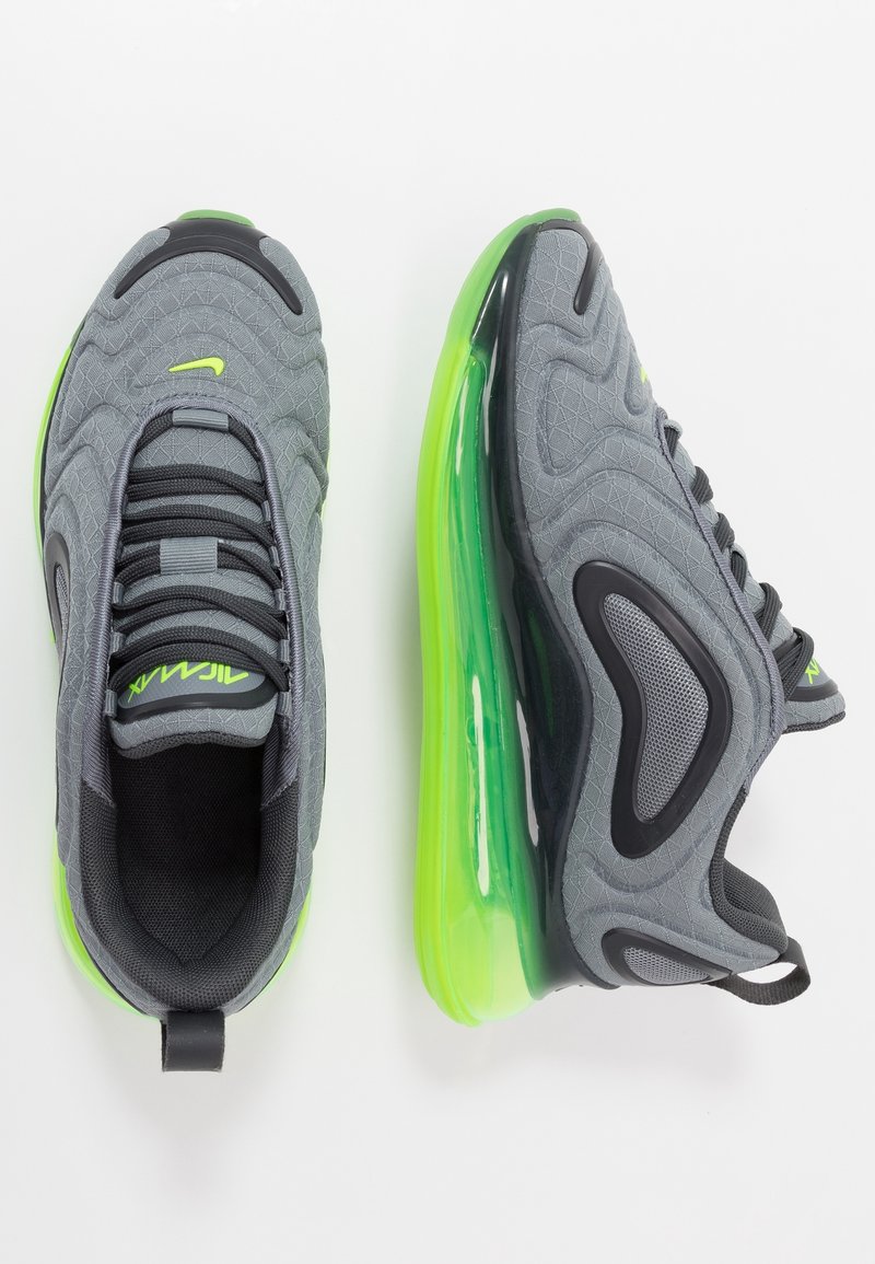 Grå atletiska skor med en texturerad ovandel, svarta detaljer och en livlig grön luftkuddessula. Har snörning och en ögla vid hälen.