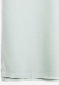 Ljust grönt texturerat bomullstyg som visar en slät yta med en fållad botten och sidoklyftor för ökad rörlighet.