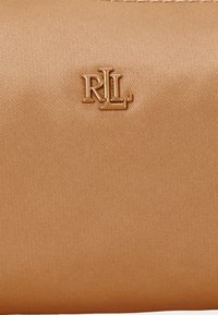 Bež najlon torbica z embosiranim zlatim logotipom "RL". Površina je gladka z rahlim leskom, kar dopolnjuje minimalističen dizajn.