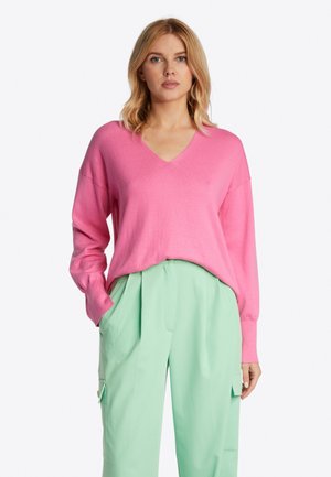 Rosa V-Ausschnitt Pullover mit langen Ärmeln, lockerer Passform und weicher Textur, kombiniert mit mintgrünen, gefalteten Hosen mit Seitentaschen.