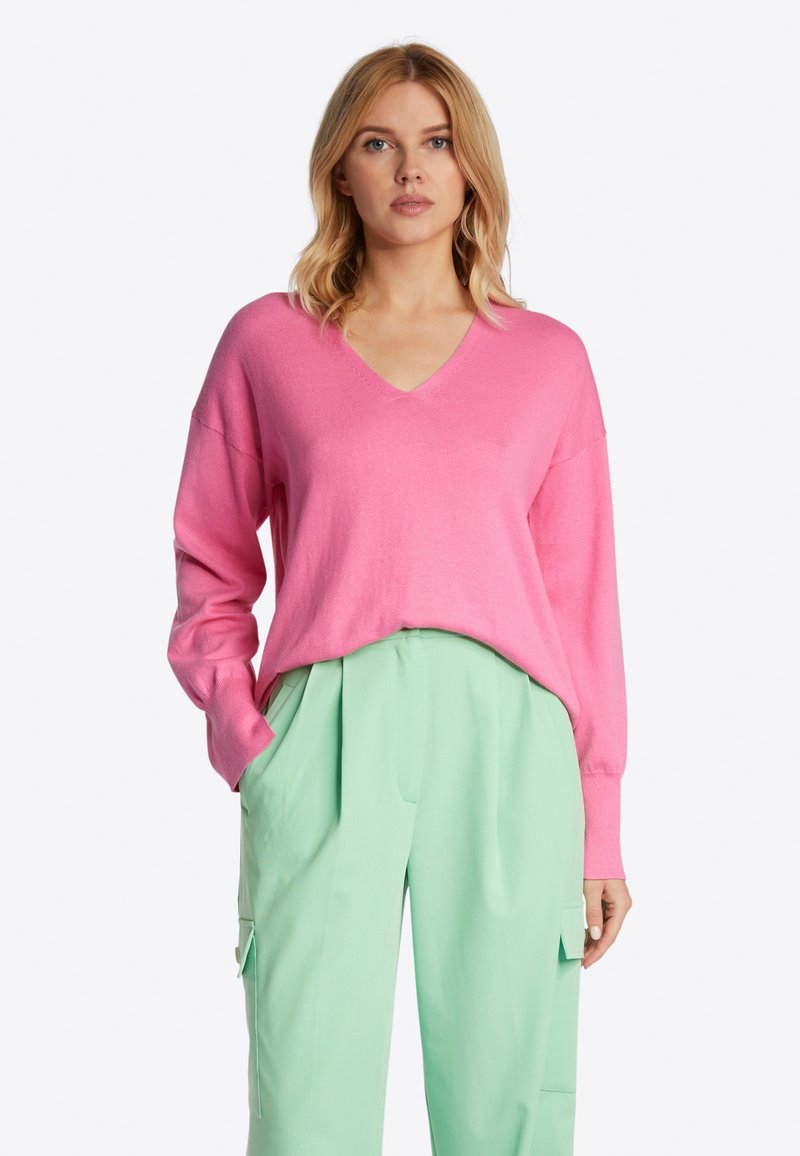 Rosa V-Ausschnitt Pullover mit langen Ärmeln, lockerer Passform und weicher Textur, kombiniert mit mintgrünen, gefalteten Hosen mit Seitentaschen.