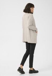 Beige lange mouw trui met een relaxte pasvorm, zijzakken en een rechte snit, gecombineerd met zwarte slim-fit broek en zwarte schoenen.