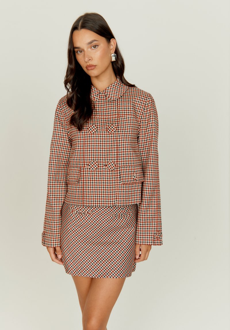 Ελέγχου, κόκκινο και πράσινο σακάκι με γιακά και διπλό μπροστινό μέρος, συνδυασμένο με φιλικό εφαρμοστό φούστα. Λείο υφασμάτινο texture.