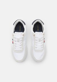 Zapatillas blancas con un upper sintético suave, detalles en ante color crema, forro azul marino y tres franjas en rojo, blanco y azul en los laterales.