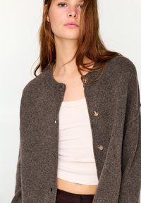 Bruine wollen cardigan met een ronde hals, voorzien van drie knopen aan de voorkant, licht oversized pasvorm en zachte textuur.