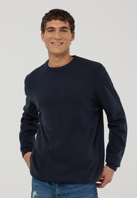 Maglione di lana blu navy con scollo rotondo e polsini a costine, abbinato a jeans celesti. Caratterizzato da una vestibilità comoda e una texture liscia.
