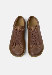 Sneakers in pelle marrone con lacci piatti, punta tonda e dettagli di cucitura sottili. Suola in gomma con finitura testurizzata.