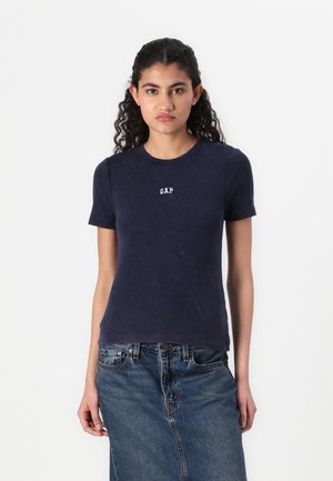 Marineblå ribbestrikket t-skjorte med korte ermer og rund hals, med en hvit "GAP"-logo på brystet, båret sammen med en denimskjørt.