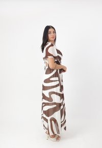 Braun- und weiß gemustertes Maxikleid mit kurzen Ärmeln, tailliertem Bund und fließendem Stoff. Kombiniert mit Absatzsandalen.