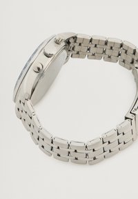 Ασημένιο μεταλλικό ρολόι χειρός με στρογγυλό καντράν, υφασμένο bezel και βραχιόλι με συνδέσεις. Περιλαμβάνει κορώνα για ρυθμίσεις και λείο φινίρισμα.