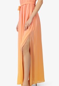 Maxi-jurk in een verloop van perzik naar oranje stof, met een zijslit, een strakke taille met een bijpassende riem en een soepele, vloeiende textuur.
