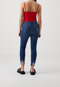 Úzké modré džíny s vysokým pasem, zdobené roztrhanými detaily na lemech. Kombinovány s červeným tílkem a černými sandály.