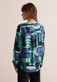 Långärmad blus med ett geometriskt mönster i grön, blå och svart. Mjuktyg med veckdetalj på baksidan och knäppte ärmslut.