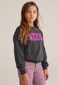 Szürke pulóver élénk rózsaszín "Cherish" felirattal, rózsaszín leopárd mintás nadrággal párosítva. Puha pamut anyagból készült, laza fazonú és bordázott mandzsettákkal rendelkezik.