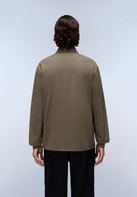 Olijfgroene blouse met lange mouwen, een relaxte pasvorm, zachte textuur en een kraaghals, gedragen met zwarte cargobroeken.