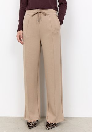 Beige wide-leg trousers with drawstring waist worn with brown long-sleeve top and zebra-patterned high-heeled shoes.