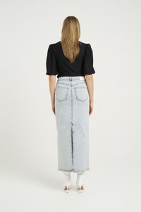 Svart topp med pufferm parret med en høy midje, lys blå denim maxiskjørt med åpning bak og sømdetaljer, supplert med hvite hæler.