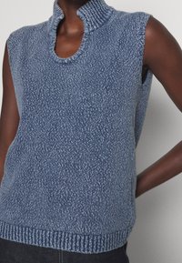Suéter sin mangas de textura en azul marino con cuello alto y escote redondeado. Presenta un dobladillo acanalado y un sutil patrón moteado.