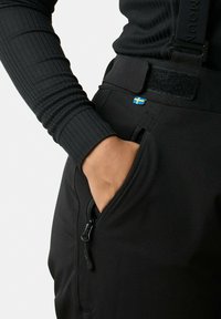Zwarte broek met een ritszak, elastische tailleband en verstelbare bretels, gemaakt van een gestructureerde stof, met een klein Zweeds vlaggetje.