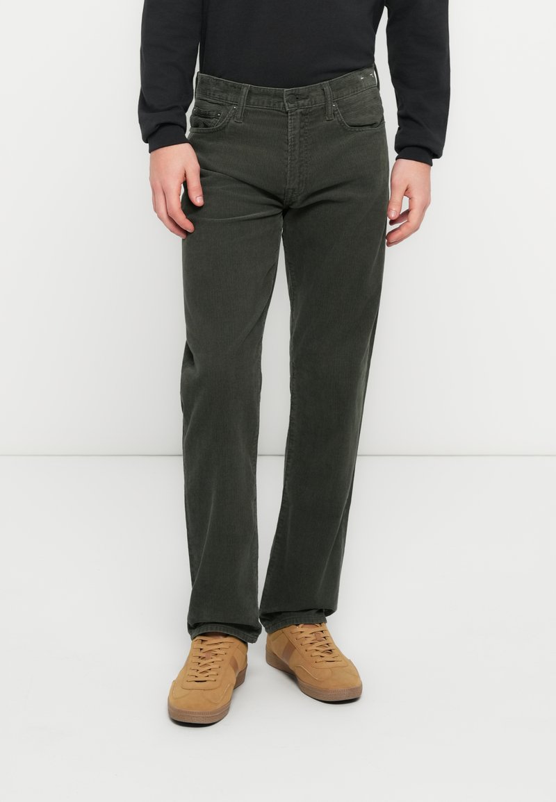 Jean vert foncé à jambes droites avec un tissu texturé, cinq poches et des ferrures en métal, associé à des baskets marron clair.