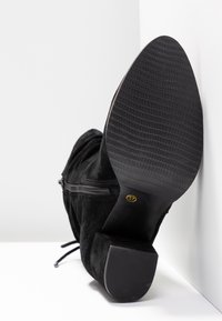 Bottine en suède noir avec semelle en caoutchouc texturée, fermeture éclair latérale et talon carré. Taille 37 indiquée sur la semelle.