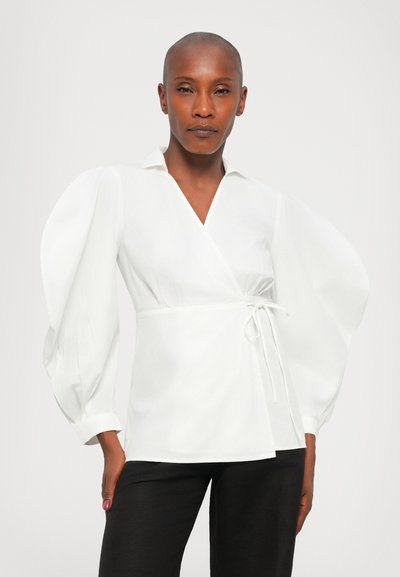 Witte wikkelblouse met pofmouwen, strikdetail bij de taille en een puntige kraag. Gladde textuur, ontworpen met een relaxte pasvorm.