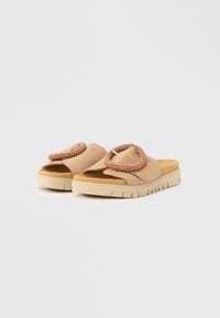 Beige Sandalen mit einem weichen Wildleder-Obermaterial, gestaltet mit einem übergroßen runden Akzent aus Perlen. Dicke Sohle mit geriffelter Textur für besseren Halt.