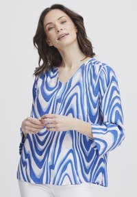 Bluză albastră și albă cu un model ondulat, material ușor, decolteu în V, mâneci trei sferturi și o croială lejeră.