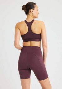 Burgundin urheilusetti, joka sisältää hihattoman, urheilullisen topin sekä yhteensopivat korkeavyötäröiset pyöräilyshortsit, joissa on litteät saumat ja taskut.