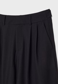 Zwarte broek met een rechte voorkant, twee zijzakken en plooien voor extra textuur. Gemaakt van een gladde, op maat gemaakte stof.