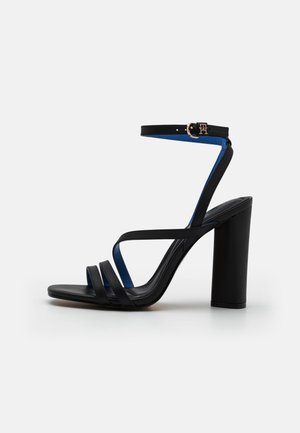 Sandale à talons en cuir noir avec trois brides horizontales et une doublure intérieure bleue. Elle dispose d'une fermeture à boucle et d'un design de talon épais.