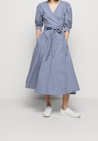 Blå och vit rutig klänning med omslagsdesign, puffärmar och ett knytbälte. Har en full kjol och sidofickor. I kombination med vita sneakers.