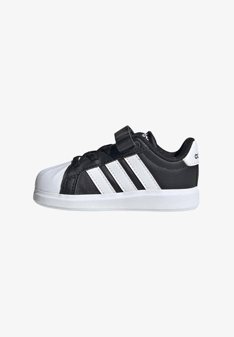 Scarpa da ginnastica Adidas in bianco e nero con tre strisce bianche, cinturino in velcro, lacci neri, suola bianca e punta arrotondata.