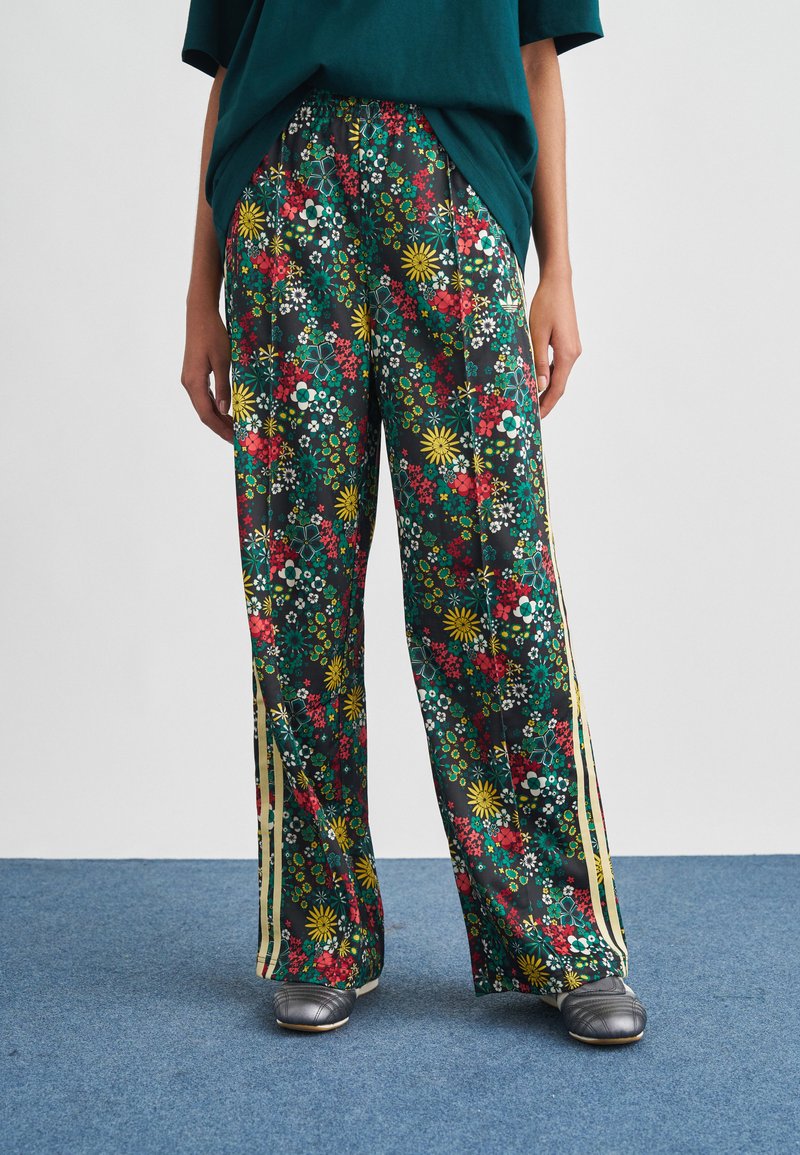 Floral printed wide-leg trousers with green, red, and yellow flowers on a black background. Features side stripes and elastic waistband.