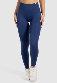 Leggings blu navy con fascia alta in vita, realizzati in tessuto elastico. Finitura liscia senza motivi o dettagli visibili, abbinati a scarpe da ginnastica bianche.