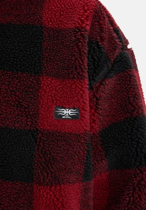 Red and black plaid fleece jacket, featuring a textured surface and a logo patch on the front. Soft, cozy material suitable for warmth.