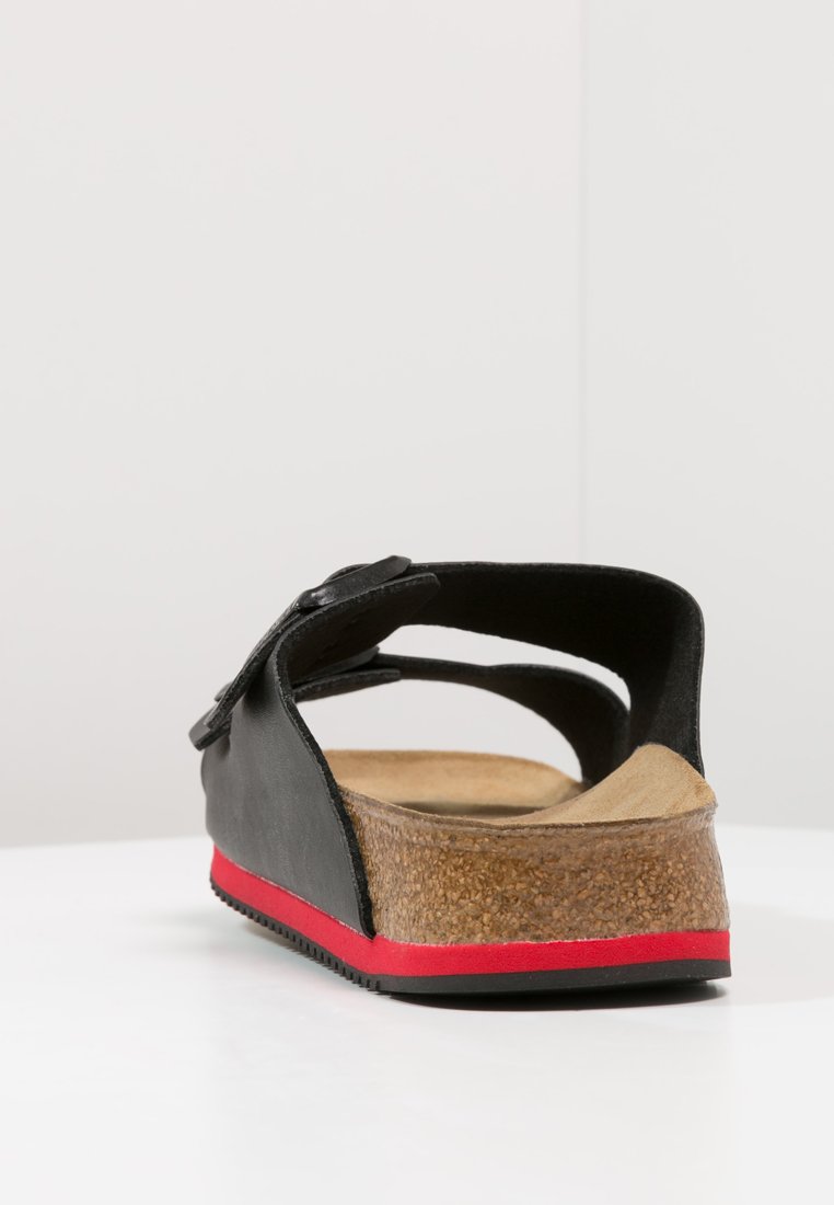 Black sandal with adjustable strap, cork footbed, and red accent on the rubber outsole. Sleek design with an open back.